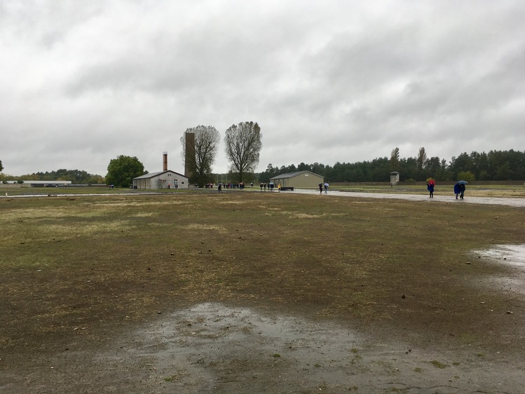 A brown and muddy field, with a fence and watchtower visible on the horizon.